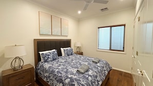 A bedroom with a bed, nightstands, a lamp, a ceiling fan, and a window with blinds. - Captains Cottage SWR (SOUTH WEST ROCKS)