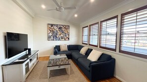 A living room with a sectional sofa, a flat-screen TV, a coffee table, and a ceiling fan. - Captains Cottage SWR (SOUTH WEST ROCKS)