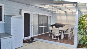 Eine überdachte Terrasse mit Tisch, Stühlen, einem Grill und einer Glasschiebetür, die zu einer Garage führt.
