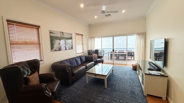 A living room with a leather sofa, a coffee table, a TV, and a balcony with a view. - Captains Cottage SWR (SOUTH WEST ROCKS)