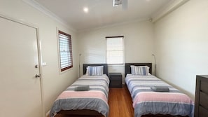 A bedroom with two single beds, a door, and two windows with blinds. - Captains Cottage SWR (SOUTH WEST ROCKS)