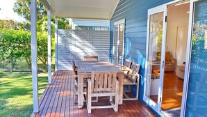 A covered patio with a wooden table and chairs, a sliding glass door leading to an interior space, and a blue exterior wall.