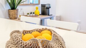 A kitchen with a coffee machine, a potted plant, and a basket of oranges on the table.
