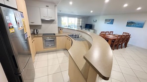 A modern kitchen with a built-in oven, a refrigerator, and a sink. There is a dining area with wooden chairs and a table.