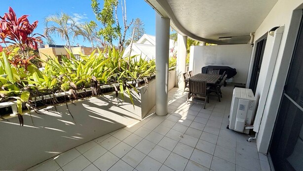 A covered patio with a tiled floor, a table and chairs, and potted plants. - Jubilee Apartment 04 (South West Rocks)
