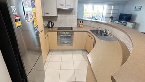 A kitchen with a refrigerator, oven, sink, and tiled backsplash. - Jubilee Apartment 04 (South West Rocks)