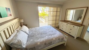 A bedroom with a bed, dresser, mirror, and a view of the outdoors. - Jubilee Apartment 04 (South West Rocks)