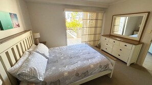 A bedroom with a bed, dresser, mirror, and a view of the outdoors. - Jubilee Apartment 04 (South West Rocks)