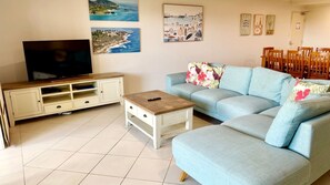 A living room with a TV, sofa, coffee table, and artwork on the wall. - Jubilee Apartment 04 (South West Rocks)