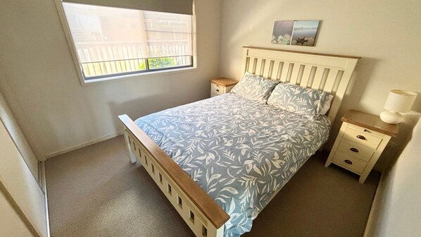 Une chambre à coucher comprenant un lit, une table de chevet, une commode, une fenêtre et un tableau accroché au mur.