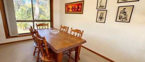 A dining room with a wooden table and chairs, a window with curtains, and wall-mounted artwork.