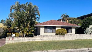 A single-story house with a red-tiled roof, a brick exterior, and a small front yard with a lawn and a palm tree.