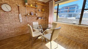A room with a brick wall, a round glass table with chairs, a clock, and shelves with various items.