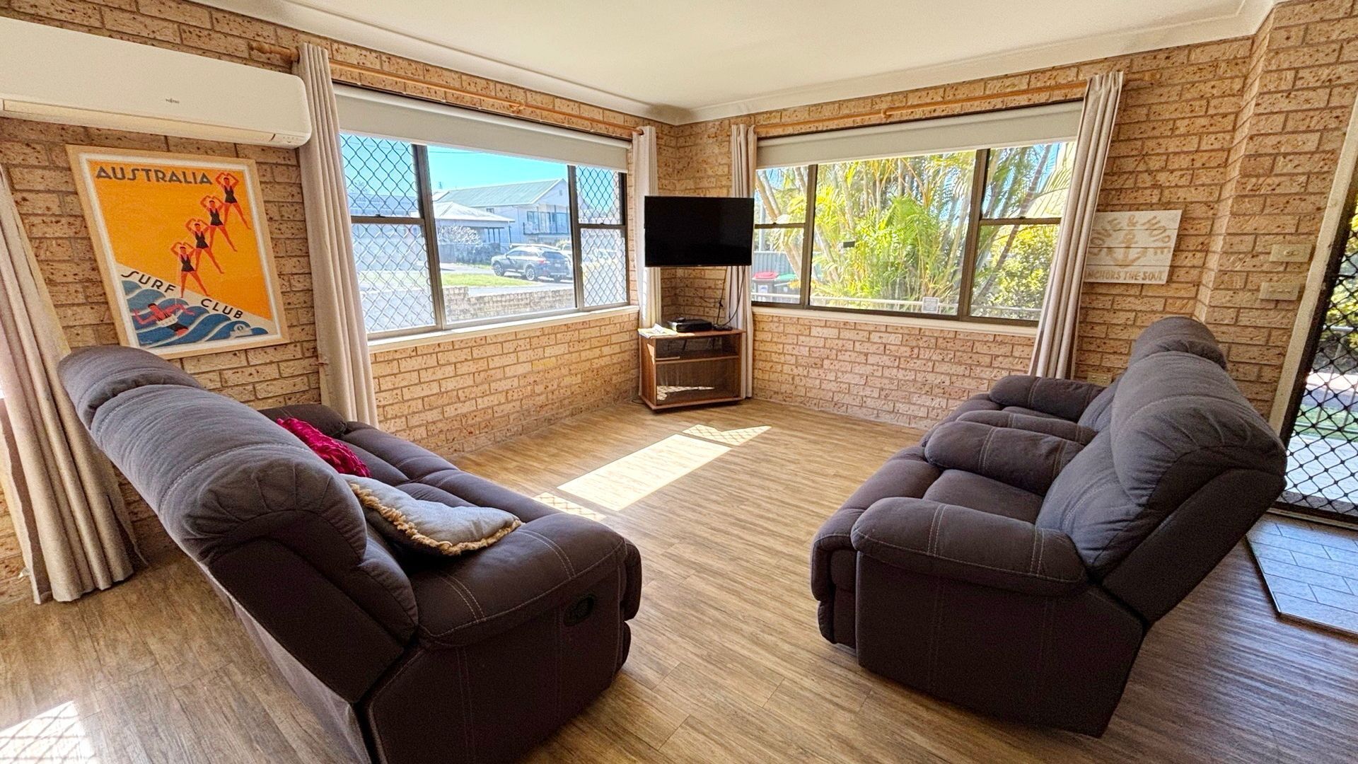 A room with two reclining sofas, a flat-screen TV, and large windows with a view of the outside.