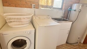 A compact laundry area with a front-loading washing machine, a dryer, and a small sink.