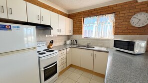 A kitchen with white cabinets, a stove, a microwave, and a window with curtains.