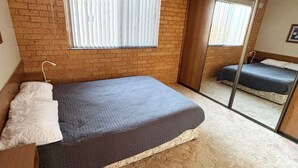 Ein Schlafzimmer mit Backsteinwand, einem Bett mit grauem Matratze, einem weißen Kopfkissen und einer Pendelleuchte.