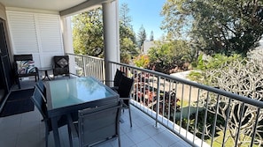 A balcony with a glass table, chairs, and a small round table with a cushion. - Jubilee Apartment 11 - Bring your own linen (SOUTH WEST ROCKS)