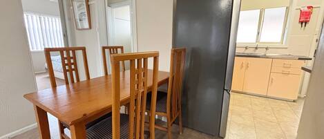 A dining area with a wooden table and chairs, a black refrigerator, and a kitchen with cabinets and a sink.