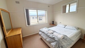 Un dormitorio con cama, cómoda de madera, ventana y mesita de noche con lámpara.