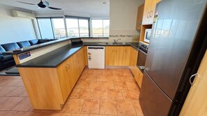 A kitchen with wooden cabinets, a built-in dishwasher, a stainless steel refrigerator, and a large window providing a view of the outside.