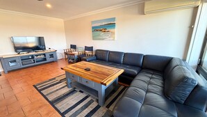 A modern living room with a black leather sofa, a wooden coffee table, a flat-screen TV, and a painting of a beach scene. - Paragon Apartment 7 - walk to the beach (SOUTH WEST ROCKS)