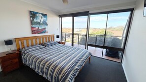 A bedroom with a bed, a nightstand, a painting, and a balcony with a view.
