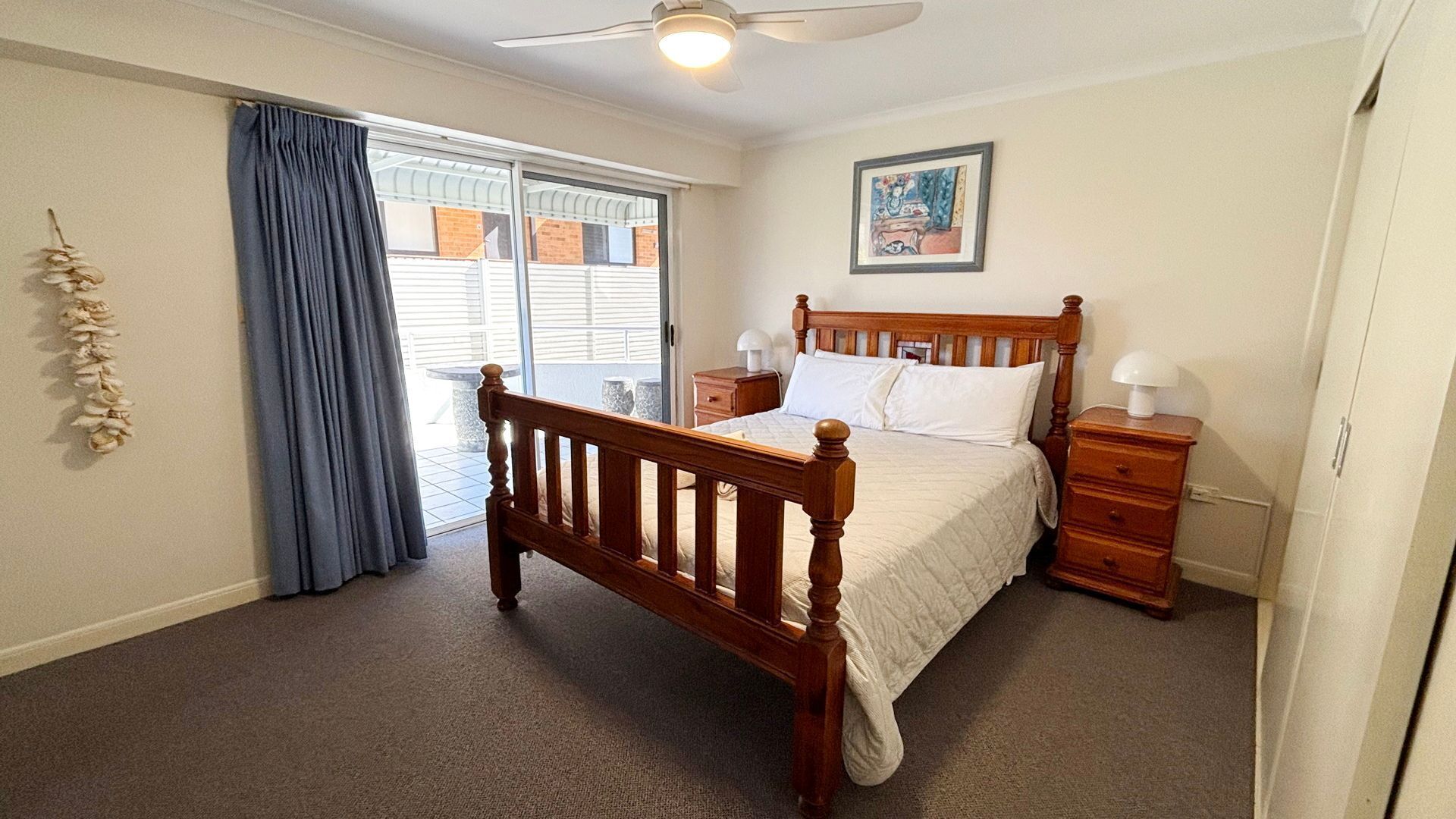 A bedroom with a wooden bed, a nightstand, a dresser, a ceiling fan, and a window with curtains.