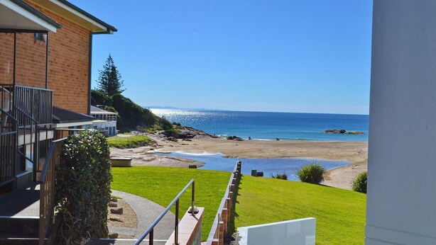 A coastal view from a balcony overlooking a beach with a clear sky. - Ocean Shores Apartment 13 (SOUTH WEST ROCKS)