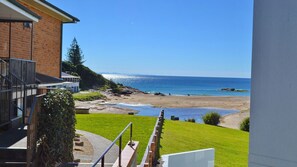 A coastal view from a balcony overlooking a beach with a clear sky. - Ocean Shores Apartment 13 (SOUTH WEST ROCKS)