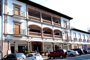 A building with a balcony, a sign reading "POSADA DEL SOL", and several parked cars in front.