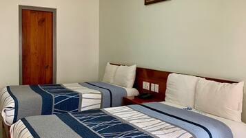 A double room with two beds, each with a patterned bedspread, a wooden headboard, and a bedside table with a lamp.