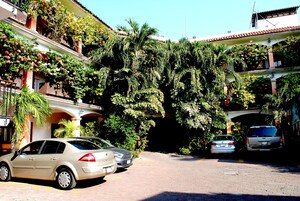 A building with multiple balconies, some with plants and flowers. There are cars parked in front.
