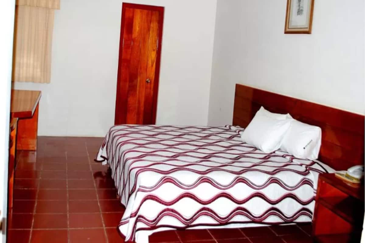 Une chambre à coucher avec un cadre de lit en bois, une couvre-lit à motifs rouges et blancs, une porte en bois et une petite table de chevet.