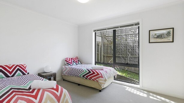 A bedroom with two beds, a window with a view of a fence, and a framed picture on the wall.