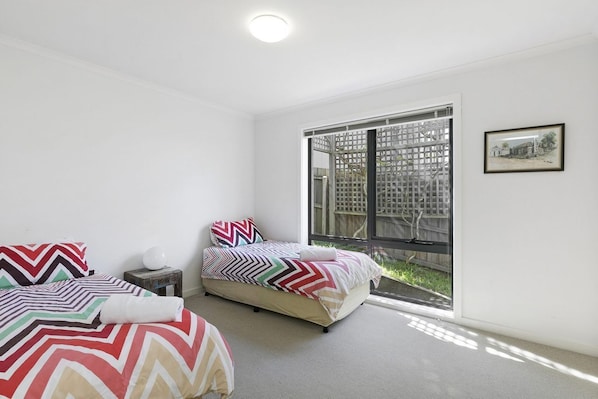 A bedroom with two beds, a window with a view of a fence, and a framed picture on the wall.