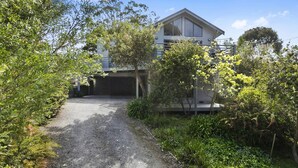 A modern house with a covered driveway, surrounded by lush greenery and trees.