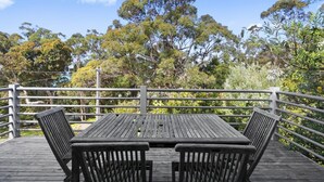 A wooden deck with a table and chairs, surrounded by a metal railing, overlooking a dense forest.