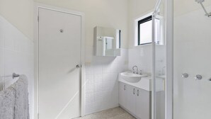 A bathroom with a white door, a sink, a mirror, and a shower area.