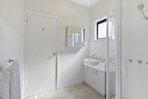A bathroom with a white door, a sink, a mirror, and a shower area.