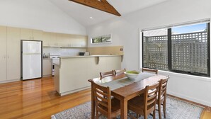 A modern kitchen with wooden beams, a dining area with a table and chairs, and a large window with a view of a fence.