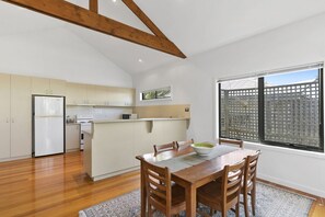 A modern kitchen with wooden beams, a dining area with a table and chairs, and a large window with a view of a fence.