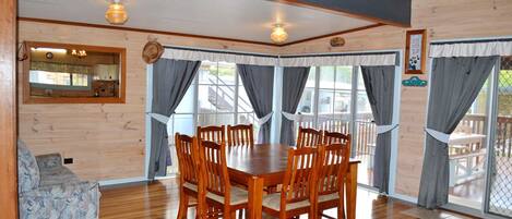 A wooden dining room with a table and chairs, a sofa, and a window with curtains.