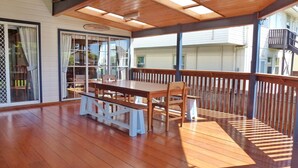 A covered patio with a wooden table and benches, large sliding glass doors, and a view of a residential area.