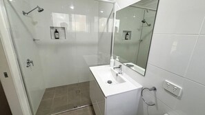 Un bany modern amb una cabina de dutxa de vidre, un lavabo blanc i un mirall.