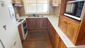 Cucina compatta con mobili in legno, un piano di lavoro bianco, un fornello, un lavandino e un forno a microonde.