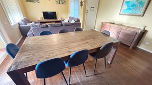 Zona pranzo con tavolo in legno, quattro sedie, un divano e una televisione sullo sfondo.