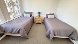 Ein Schlafzimmer mit zwei Einzelbetten, einem Nachttisch mit Lampe und einem Fenster.
