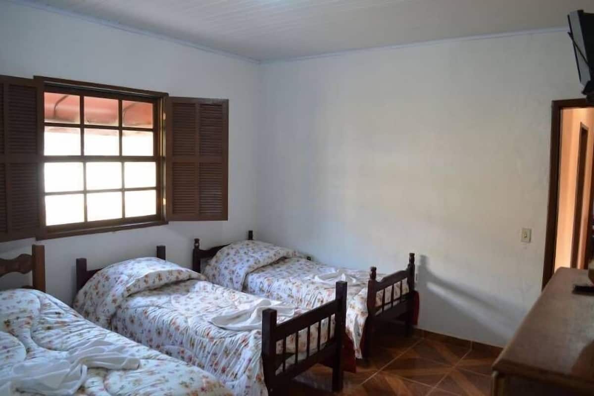 A room with two wooden beds, a window with shutters, and a tiled floor.