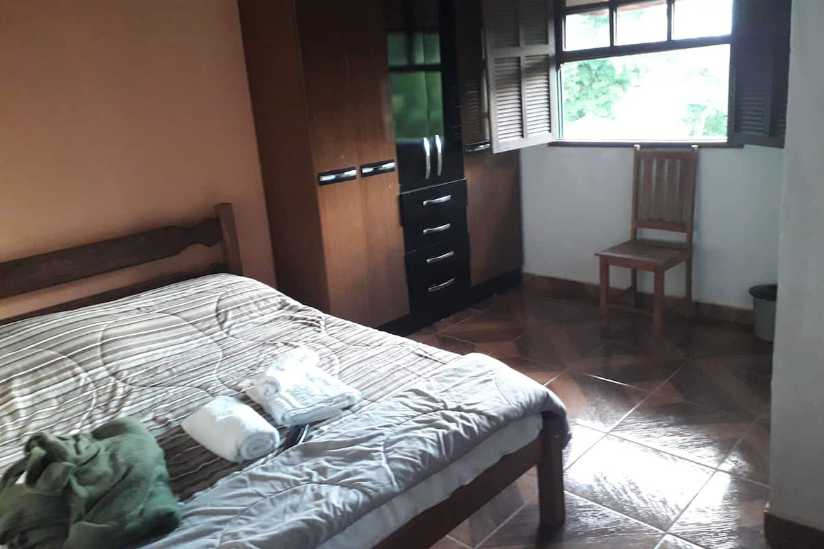 A bedroom with a bed, a wardrobe, a chair, and a window with blinds.